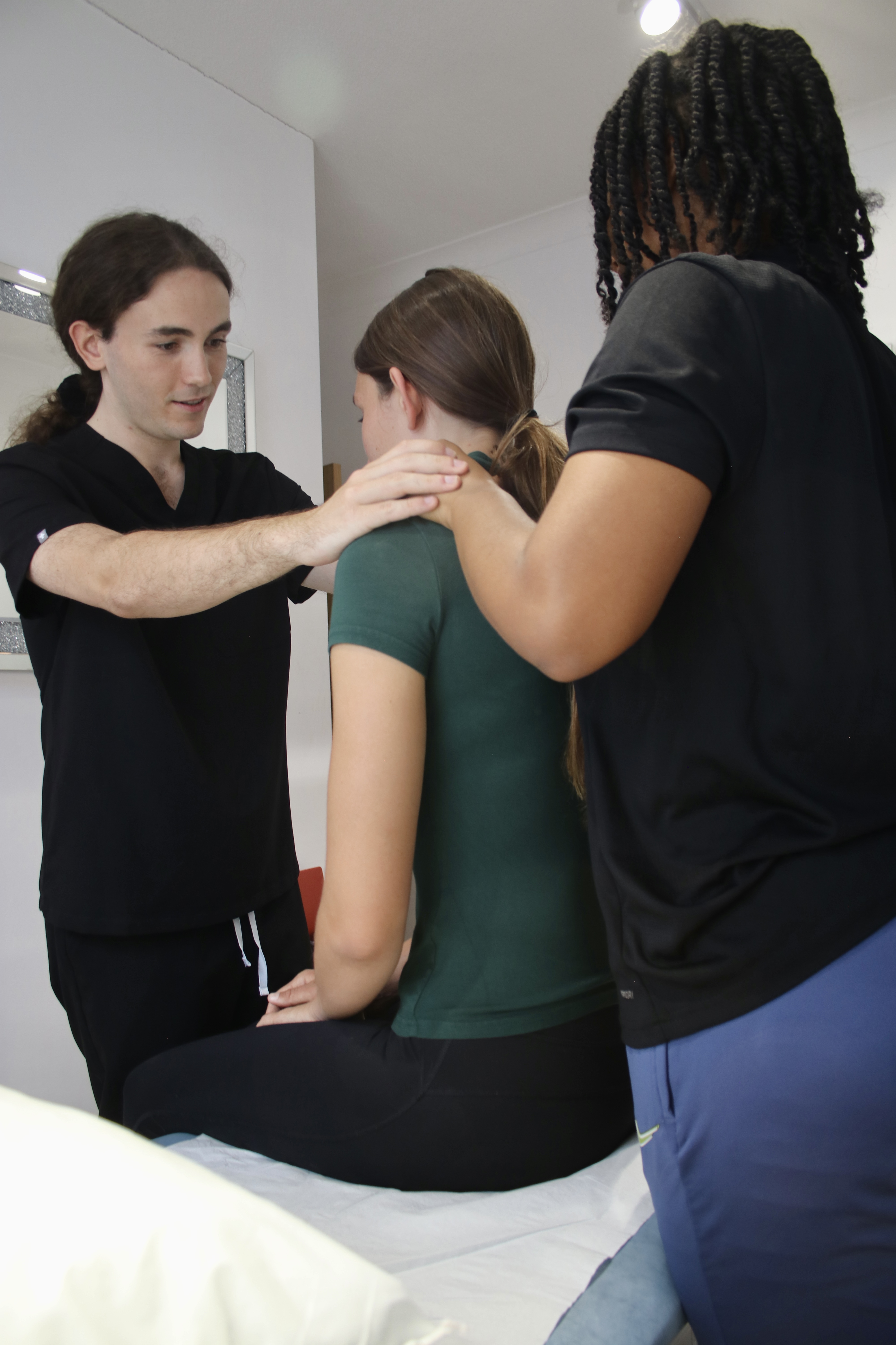 Barry osteopath showing black woman how to massage her friends shoulder